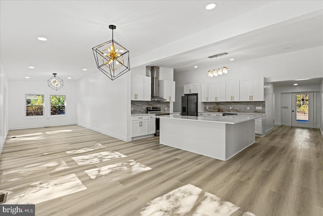 kitchen with a kitchen island, wall chimney range hood, white cabinets, pendant lighting, and appliances with stainless steel finishes