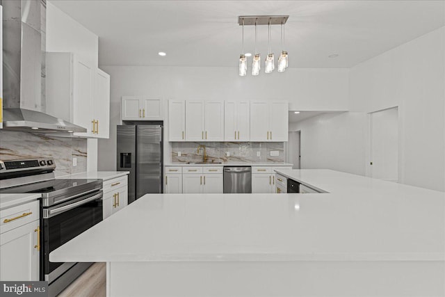 kitchen with wall chimney range hood, stainless steel appliances, decorative light fixtures, white cabinetry, and tasteful backsplash