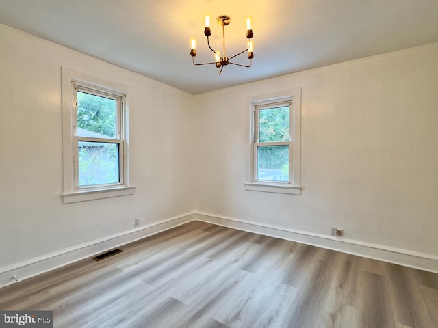 spare room with a chandelier, wood-type flooring, and a wealth of natural light