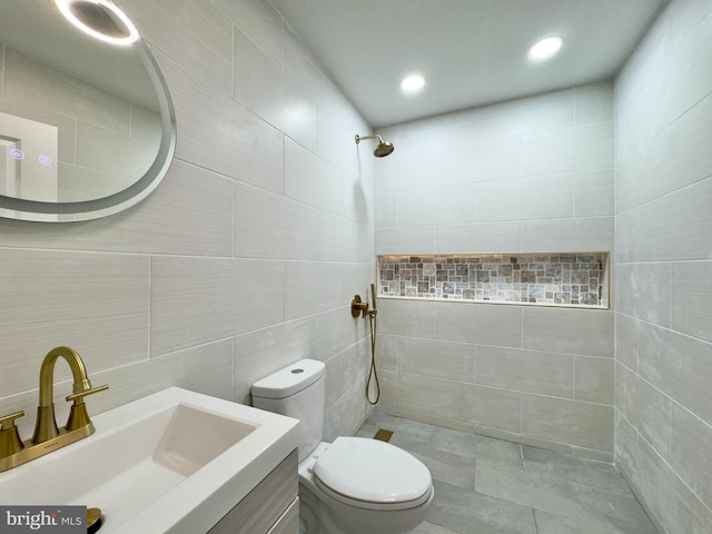 bathroom with tiled shower, tile patterned floors, toilet, tile walls, and vanity