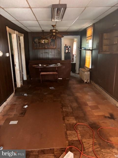 unfurnished dining area featuring wood walls, ceiling fan, and a paneled ceiling