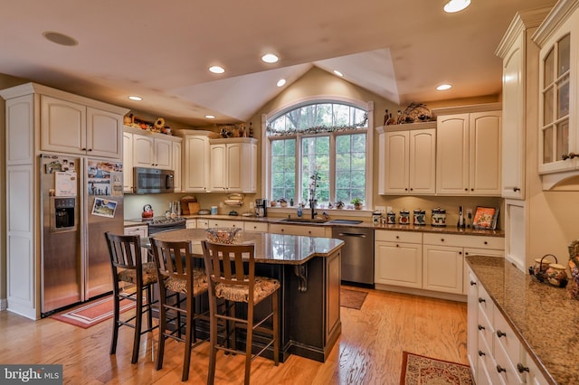 kitchen with appliances with stainless steel finishes, a breakfast bar, stone countertops, light wood-type flooring, and lofted ceiling