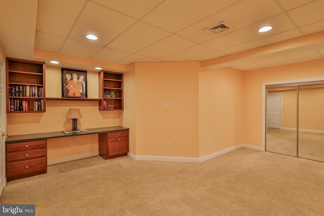 unfurnished office featuring built in desk, a paneled ceiling, and light carpet