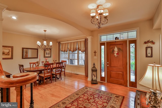 foyer with light hardwood / wood-style flooring, ornate columns, a chandelier, and crown molding