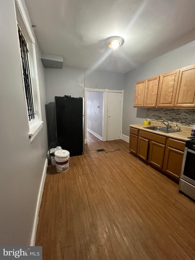 kitchen with black fridge, sink, wood-type flooring, backsplash, and stainless steel stove