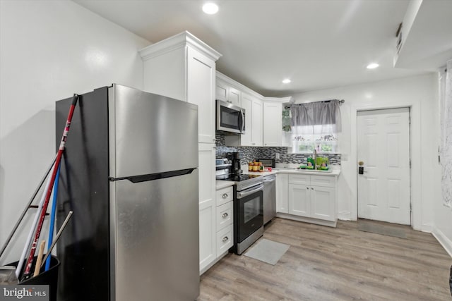 kitchen featuring appliances with stainless steel finishes, decorative backsplash, light hardwood / wood-style floors, and white cabinetry