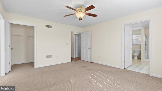 unfurnished bedroom featuring a spacious closet, light carpet, ceiling fan, and ensuite bath