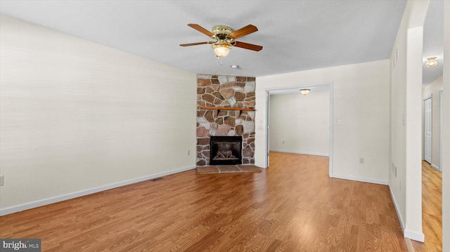 unfurnished living room featuring a stone fireplace, ceiling fan, and hardwood / wood-style flooring