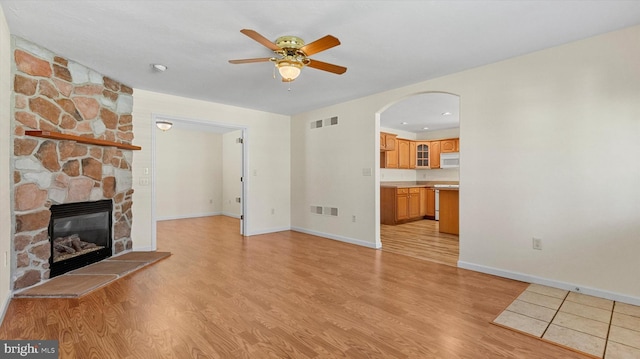 unfurnished living room with a stone fireplace, light hardwood / wood-style floors, and ceiling fan