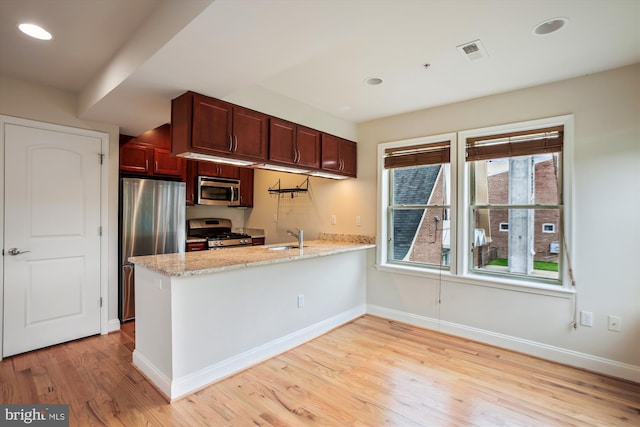 kitchen featuring light wood-type flooring, light stone counters, sink, kitchen peninsula, and appliances with stainless steel finishes