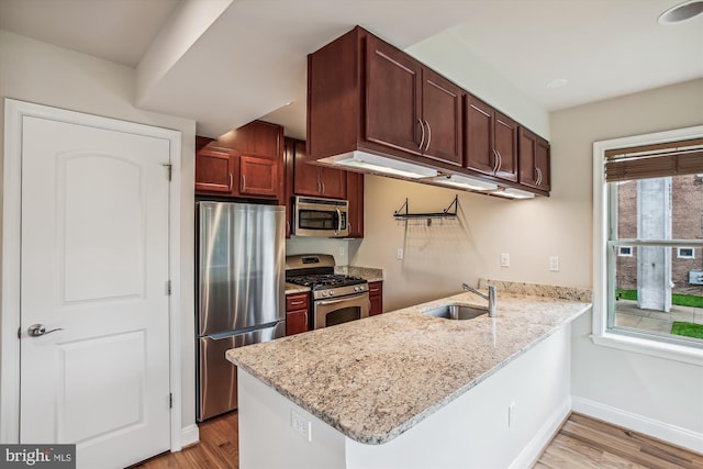 kitchen with light stone counters, sink, kitchen peninsula, light hardwood / wood-style flooring, and appliances with stainless steel finishes