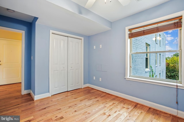 unfurnished bedroom with ceiling fan, a closet, light hardwood / wood-style floors, and multiple windows