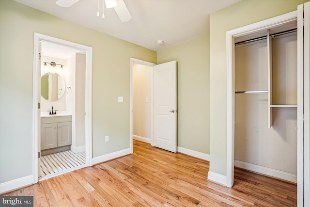 unfurnished bedroom featuring a closet, light wood-type flooring, ceiling fan, sink, and ensuite bath