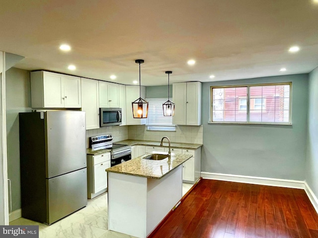 kitchen featuring appliances with stainless steel finishes, light stone counters, sink, pendant lighting, and white cabinetry