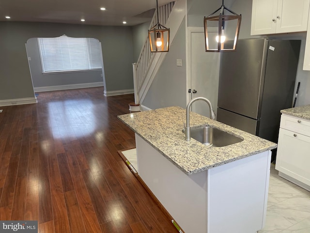 kitchen with white cabinets, stainless steel fridge, an island with sink, and pendant lighting