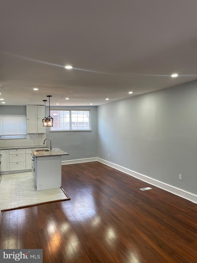 interior space with sink, dark hardwood / wood-style floors, pendant lighting, a center island with sink, and white cabinets