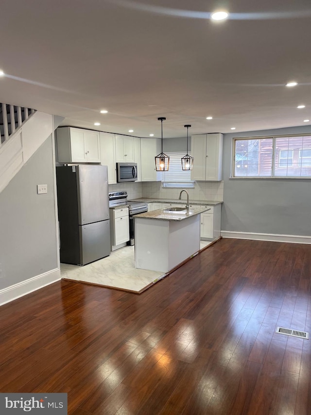 kitchen featuring white cabinets, appliances with stainless steel finishes, light stone counters, and dark wood-type flooring