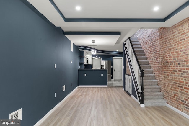 basement with light wood-type flooring, stainless steel refrigerator with ice dispenser, and brick wall