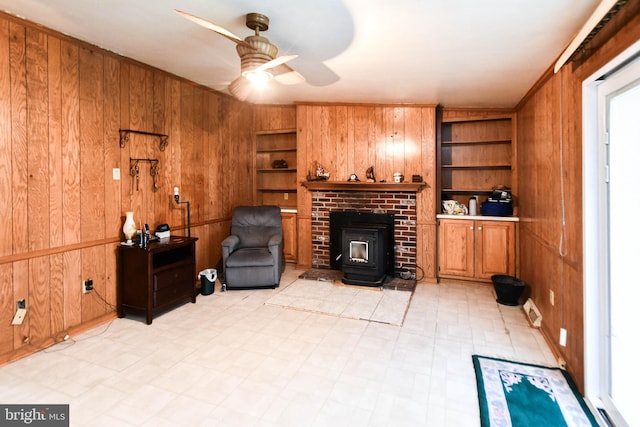 sitting room with a wood stove, wood walls, ceiling fan, and built in features