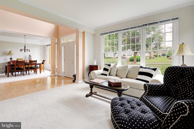 living room with ornate columns, wood-type flooring, ornamental molding, and a chandelier