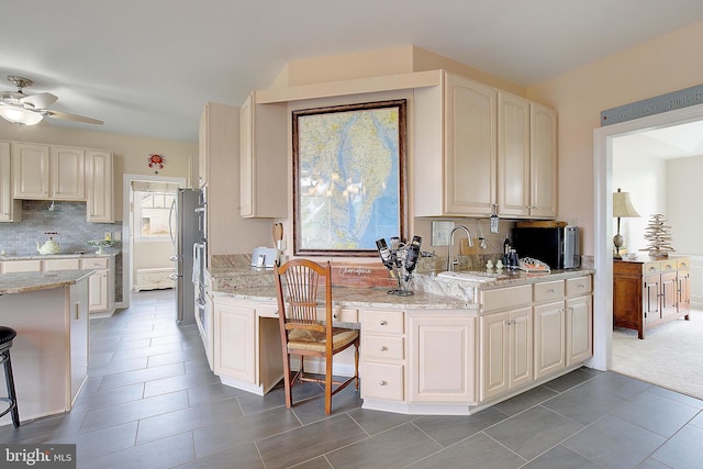 kitchen with a kitchen breakfast bar, sink, tasteful backsplash, light stone counters, and ceiling fan