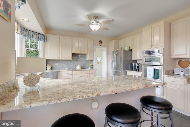 kitchen featuring light stone countertops, appliances with stainless steel finishes, backsplash, and ceiling fan