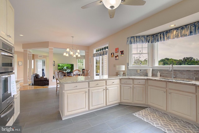 kitchen with tasteful backsplash, light stone countertops, sink, stainless steel double oven, and decorative light fixtures