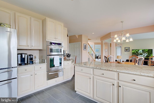 kitchen featuring hanging light fixtures, appliances with stainless steel finishes, decorative columns, a notable chandelier, and light stone counters