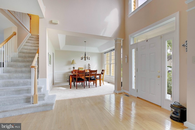 foyer with light hardwood / wood-style floors, a raised ceiling, ornate columns, and a wealth of natural light