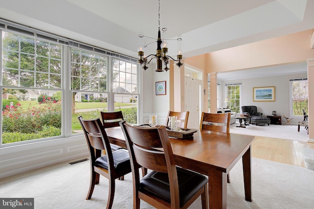 carpeted dining room with ornate columns, a healthy amount of sunlight, and an inviting chandelier