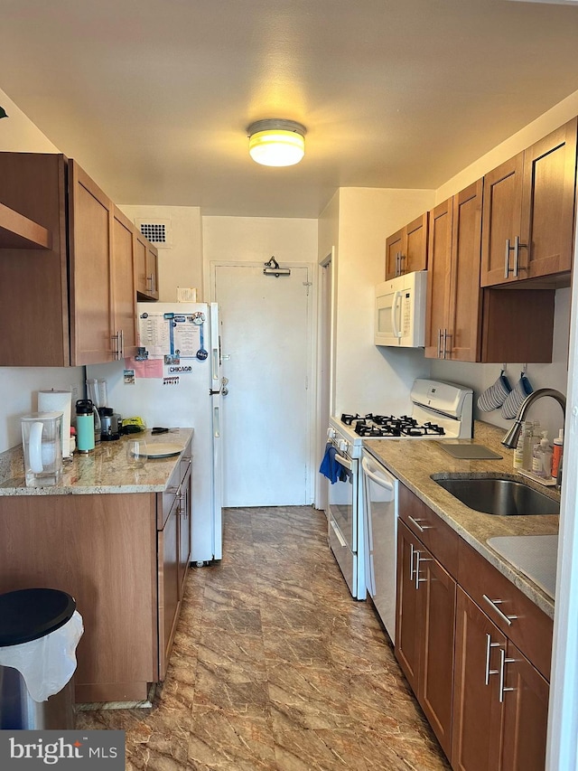 kitchen with light stone countertops, white appliances, kitchen peninsula, and sink