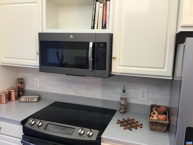 kitchen with black electric range, white cabinetry, white fridge, and backsplash