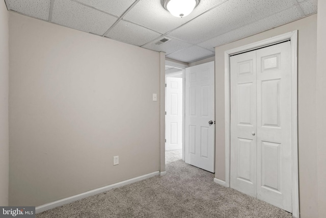 unfurnished bedroom featuring light colored carpet, a closet, and a paneled ceiling