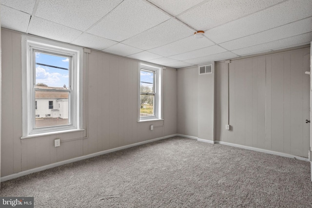 carpeted empty room with wooden walls and a drop ceiling