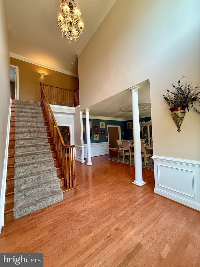 interior space with high vaulted ceiling, hardwood / wood-style flooring, decorative columns, crown molding, and a notable chandelier