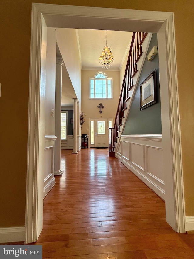 foyer entrance featuring ornamental molding, decorative columns, a notable chandelier, and hardwood / wood-style flooring