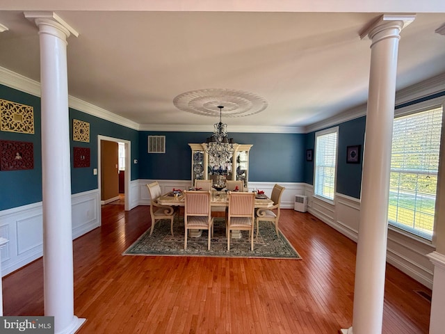 dining area featuring a notable chandelier, ornamental molding, wood-type flooring, and decorative columns