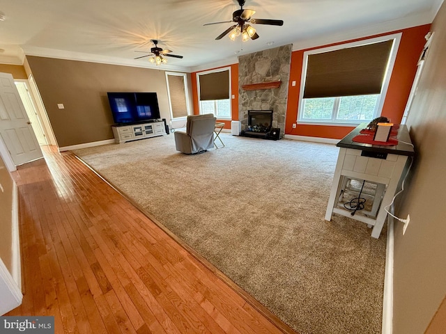 unfurnished living room with a stone fireplace, crown molding, hardwood / wood-style flooring, and ceiling fan