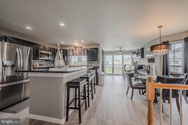 kitchen featuring pendant lighting, tasteful backsplash, stainless steel appliances, a breakfast bar area, and light hardwood / wood-style floors