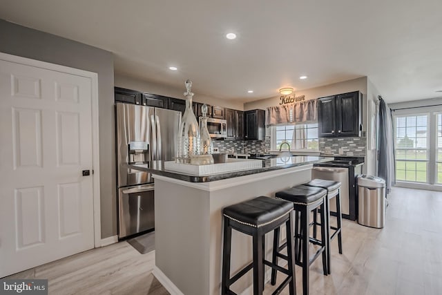 kitchen with light wood-type flooring, tasteful backsplash, a breakfast bar area, a kitchen island, and appliances with stainless steel finishes