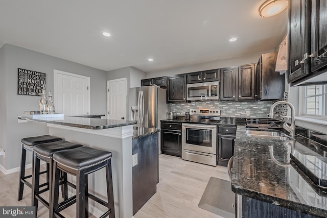 kitchen with stainless steel appliances, dark stone countertops, a center island, and sink