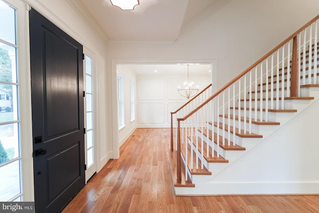 foyer featuring a healthy amount of sunlight, crown molding, light hardwood / wood-style flooring, and a notable chandelier