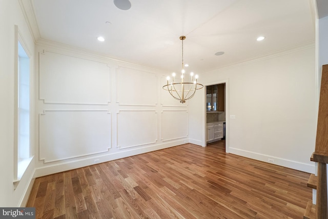 unfurnished dining area with wood-type flooring, an inviting chandelier, and crown molding