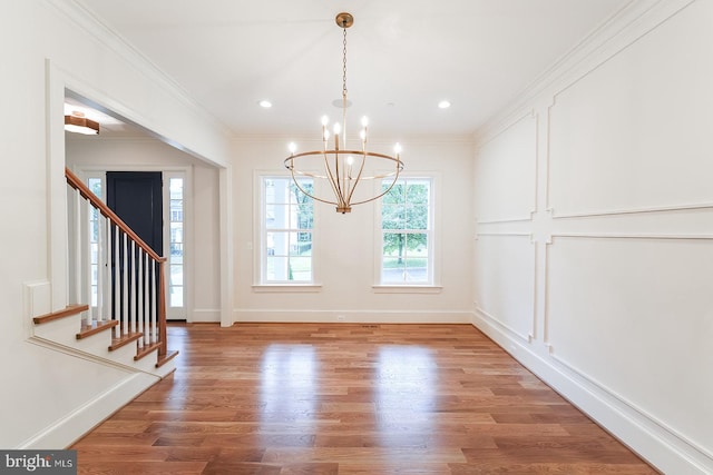 unfurnished dining area with ornamental molding, hardwood / wood-style flooring, and a chandelier