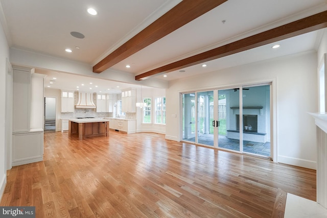 unfurnished living room with ornamental molding, light wood-type flooring, and beam ceiling