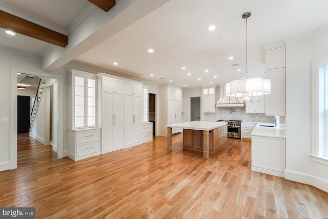 kitchen with pendant lighting, light wood-type flooring, high end stainless steel range oven, white cabinets, and a spacious island