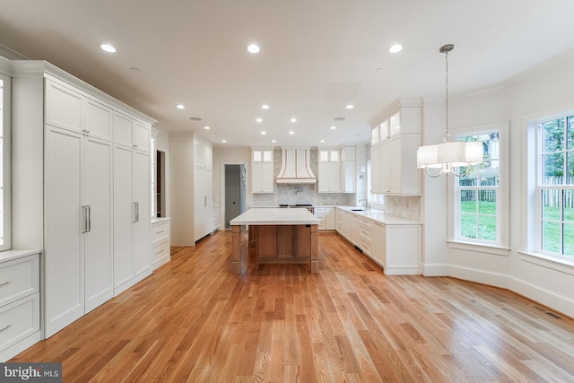 kitchen featuring light wood-type flooring, a center island, decorative light fixtures, and premium range hood