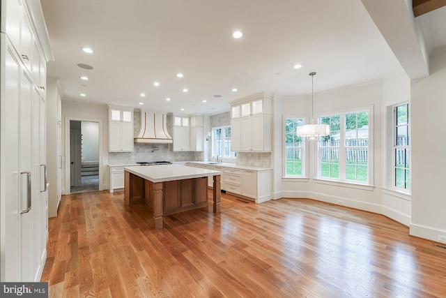 kitchen with light hardwood / wood-style floors, tasteful backsplash, white cabinets, a kitchen island, and decorative light fixtures