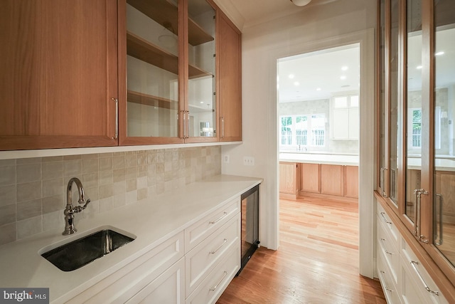 bar with white cabinets, light hardwood / wood-style flooring, sink, and decorative backsplash