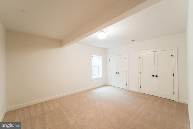 unfurnished bedroom with beam ceiling and light colored carpet